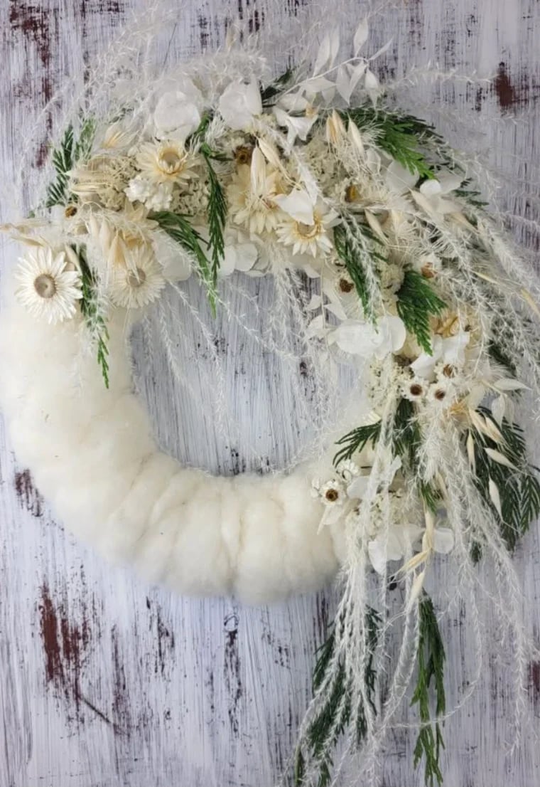 White floral wreath with daisies and green foliage on distressed wooden background