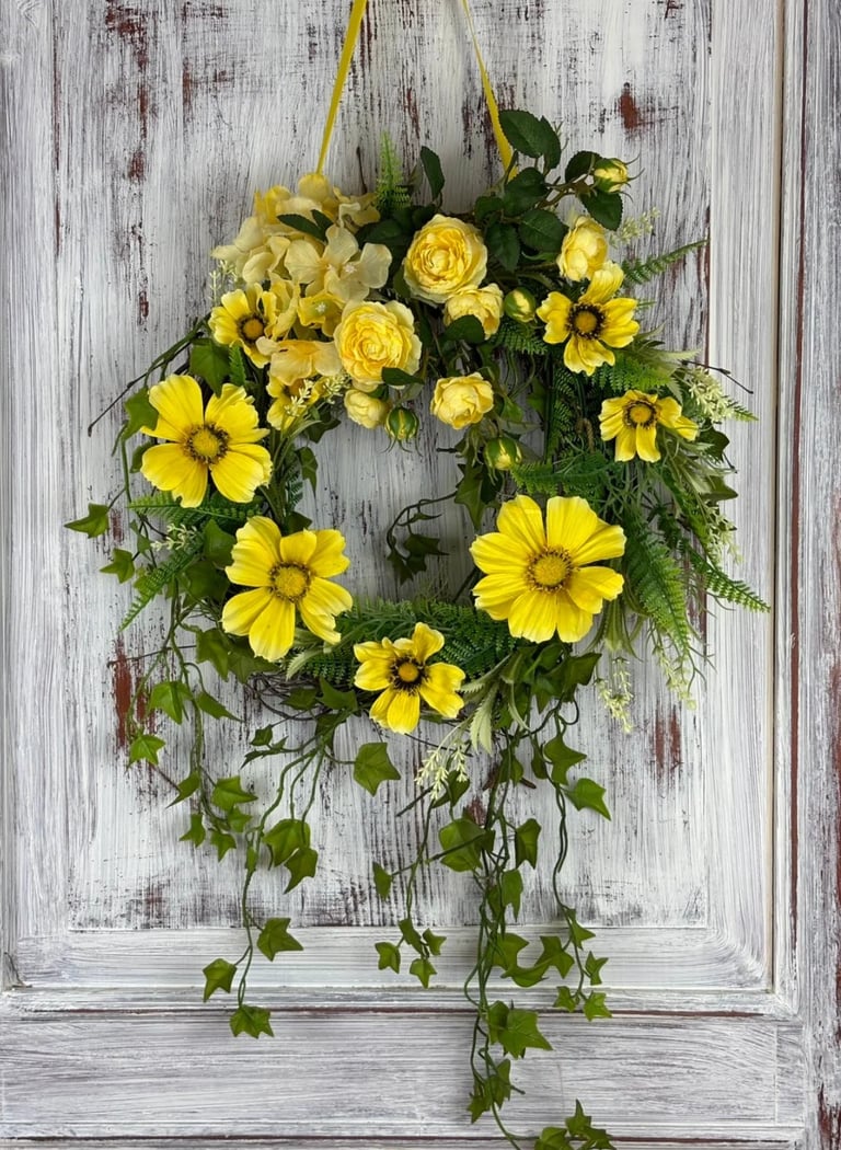 Yellow flower wreath with roses and daisies hanging on distressed white wooden door with trailing ivy
