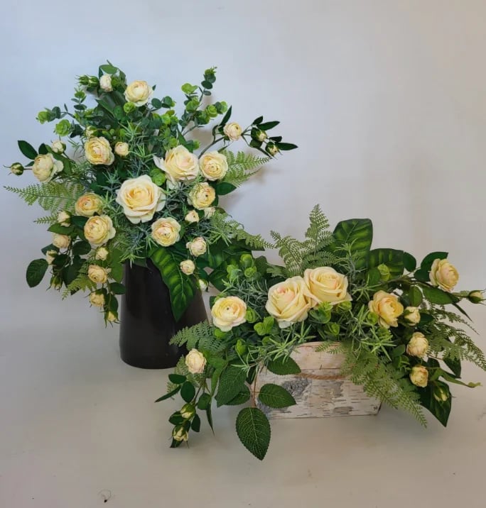 Two floral arrangements with peach roses, greenery, and ferns in a black vase and woven basket